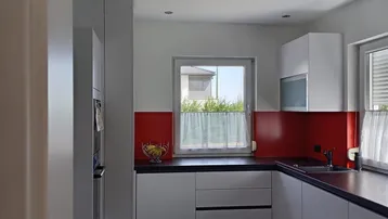 Moderne Küche mit weißen Schränken, dunkler Arbeitsplatte und rotem Fliesenspiegel.