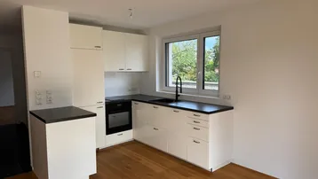 Moderne Einbauküche mit weißen Schränken, dunkler Arbeitsplatte und Fenster mit Blick ins Grüne.