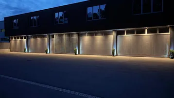 Moderne Gewerbefassade bei Nacht mit beleuchteten Garagentoren und Fenstern im Obergeschoss.