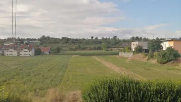Blick von einem Balkon auf weite Felder und ländliche Umgebung mit Häusern im Hintergrund.