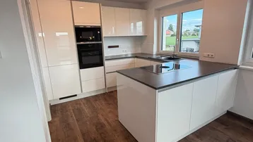 Moderne Einbauküche mit Kochinsel, glänzenden weißen Fronten und integrierten Geräten.