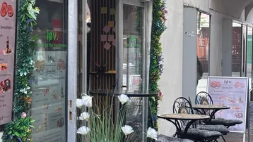 Eingangsbereich eines Cafés mit Außensitzplätzen und floraler Dekoration an der Fassade.