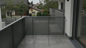 Moderner Balkon mit Fliesenboden und Glasgeländer, bietet einen Blick auf die Umgebung.