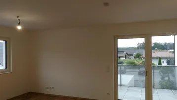 Heller Wohnbereich mit Holzboden und Zugang zu einer großen Terrasse mit Weitblick.