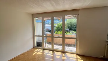 Helles Wohnzimmer mit Parkettboden und Zugang zum Balkon, bietet viel Tageslicht.