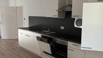 Moderne Einbauküche mit weißen Schränken, dunkler Arbeitsplatte und integrierten Geräten.