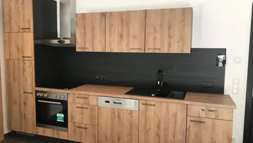 Moderne Einbauküche mit Holzfronten, schwarzer Arbeitsplatte und integrierten Geräten.