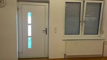 Heller Raum mit Laminatboden, weißer Tür und Fenster mit Rollläden, bereit zur Einrichtung.