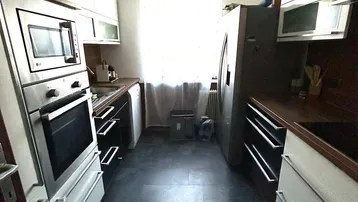 Schmale Küche mit weißen Schränken, dunklen Arbeitsplatten, Einbaugeräten und einem Fenster am Ende.