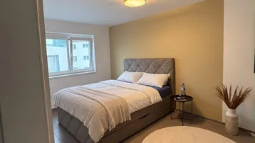 Helles Schlafzimmer mit modernem Bett, beiger Akzentwand und Fliesenboden.