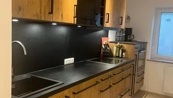 Moderne Küche mit Holzfronten, schwarzer Arbeitsplatte und integrierten Geräten, gut beleuchtet.