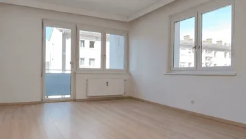 Helles Wohnzimmer mit Laminatboden, großen Fenstern und Zugang zum Balkon.