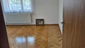 Helles Zimmer mit Fischgrätparkettboden, weiß gestrichenen Wänden und einem Fenster mit Blick ins Grüne.