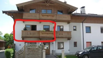 Mehrstöckiges Gebäude im alpinen Stil mit Holzbalkonen und weißer Fassade, ein SUV parkt davor.