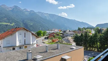Blick auf die umliegende Berglandschaft mit Häusern und einem Flachdach im Vordergrund.