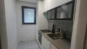 Kleine, funktionale Küche mit weißen Schränken, integriertem Herd und einem Fenster.