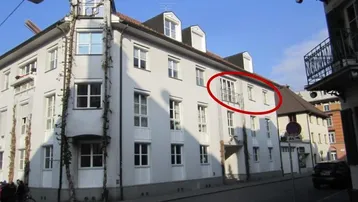 Weißes Mehrfamilienhaus mit klassischer Architektur und einem französischen Balkon an der Fassade.