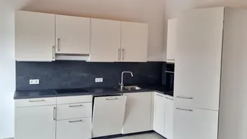 Moderne Einbauküche mit weißen Schränken, dunkler Arbeitsplatte und sichtbaren Holzbalken an der Decke.