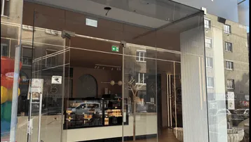 Eingangsbereich eines modernen Cafés mit großer Glasfassade und stilvollem Schriftzug.