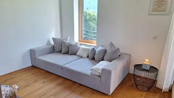 Helles Wohnzimmer mit großem, modernem Sofa und Blick auf die umliegende Landschaft und Berge.