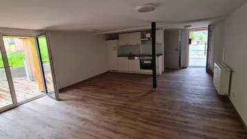 Heller offener Wohnbereich mit Holzboden, integrierter Küchenzeile und Zugang zu einer Holzterrasse.
