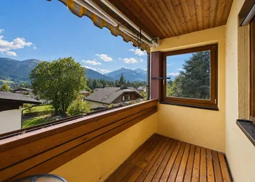 Geräumiger Balkon mit Holzboden, Markise und herrlichem Bergblick unter blauem Himmel.