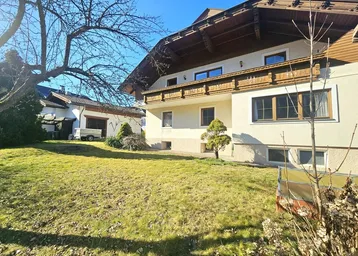 Seitenansicht des Hauses mit gepflegtem Rasen und Sträuchern unter blauem Himmel.