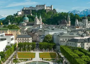 Panoramablick auf die historische Stadt Salzburg mit der Festung Hohensalzburg und gepflegten Gärten im Vordergrund.