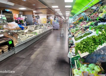 Langer Gang in einem Supermarkt mit frischem Obst, Gemüse und einer Fleischtheke. Die Fliesenböden sind sauber und die Beleuchtung hell.