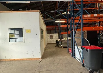 Geräumige Lagerhalle mit hohen Decken, robustem Betonboden und integriertem Büro. Die Halle zeigt deutliche Gebrauchsspuren.