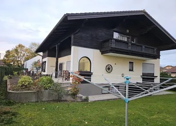 Traditionelles Haus mit Balkon, Garten und Wäschespinne unter bewölktem Himmel.