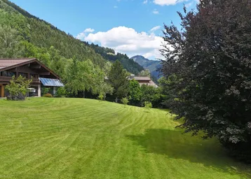 Weitläufiger grüner Garten mit gepflegtem Rasen, umgeben von Bäumen und mit Blick auf die Berge.