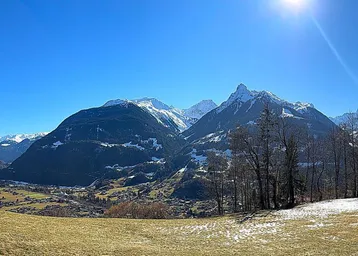 Weitläufiger Panoramablick auf schneebedeckte Berge und ein grünes Tal unter strahlend blauem Himmel.