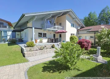Großzügiges Einfamilienhaus mit gepflegtem Garten, Terrasse und Balkon, umgeben von grüner Landschaft.