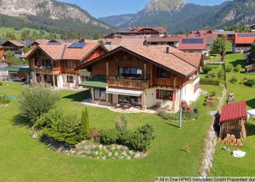 Luftaufnahme eines charmanten Hauses im alpenländischen Stil mit Bergblick und gepflegtem Garten.