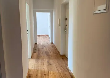 Langer Flur mit Holzdielenboden, weißen Wänden und integrierten Deckenleuchten.