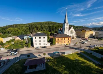 Luftaufnahme einer Stadt mit Kirche, Häusern und grünen Hügeln unter blauem Himmel.