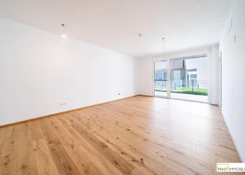 Helles, leeres Zimmer mit Holzboden und Zugang zu einem Außenbereich durch eine große Glasschiebetür.