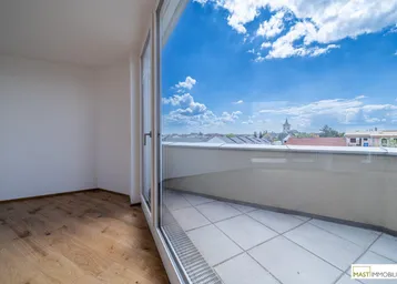 Helles Zimmer mit Holzboden und großem Fenster, das Zugang zu einem Außenbereich bietet.