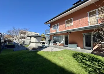Gepflegter Gartenbereich mit Rasenfläche, Steinterrasse und Außengrill hinter dem Haus.