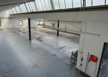 Große, leere Lagerhalle mit Betonboden, weißen Wänden und einem lichtdurchlässigen Dach für viel Tageslicht.