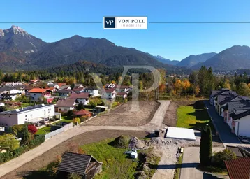 Luftaufnahme eines Baugrundstücks in einer ländlichen Umgebung mit Bergblick und umliegenden Häusern.