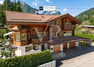 Traditionelles Holzchalet mit mehreren Balkonen, Ziegeldach und Bergblick in alpiner Umgebung.