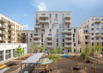 Moderne Wohnanlage mit mehreren Gebäuden, Balkonen und einem zentralen Spielplatz im Innenhof.