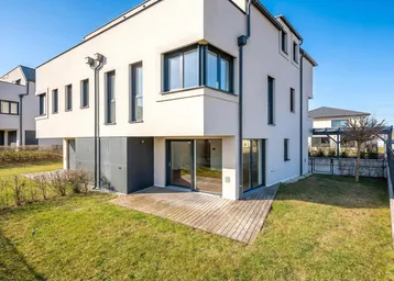 Moderne Hausfassade mit großem Garten und Holzterrasse.