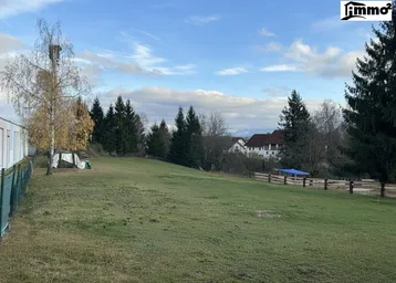 Weitläufiges grünes Grundstück mit Bäumen und einem Haus im Hintergrund unter bewölktem Himmel.