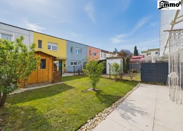 Gepflegter Garten mit Rasenfläche, Gartenhaus und Blick auf bunte Reihenhäuser.