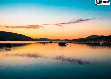 Malerischer Sonnenuntergang über einem ruhigen See mit Segelbooten und Bergen im Hintergrund.