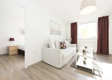 Helles Wohnzimmer mit modernem Sofa, Holzboden und Blick in ein angrenzendes Schlafzimmer.