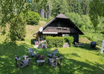 Gemütliches Holzhaus mit großem Garten und Feuerstelle, umgeben von grünen Wäldern.